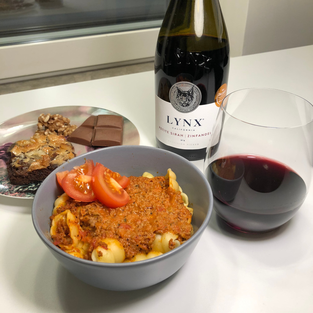 En bild på kvällens mat, en skål med pasta och köttfärssås, en assiett med kaka och choklad och en flaska vin. 
